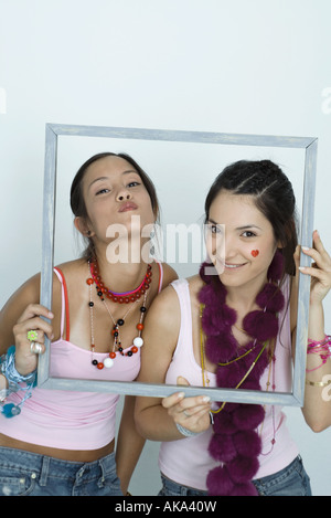 Deux jeunes femmes friends holding up photo frame, souriant et le gaufrage, portrait Banque D'Images