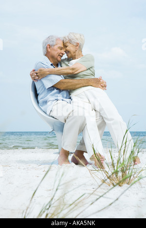 Senior couple sitting in chair on beach avec front touchant, femme assise sur les genoux de l'homme Banque D'Images