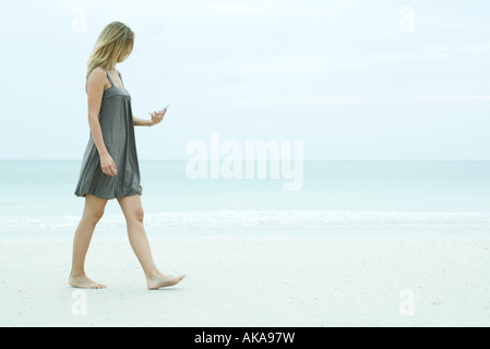 Jeune femme marchant sur la plage, looking at cell phone Banque D'Images
