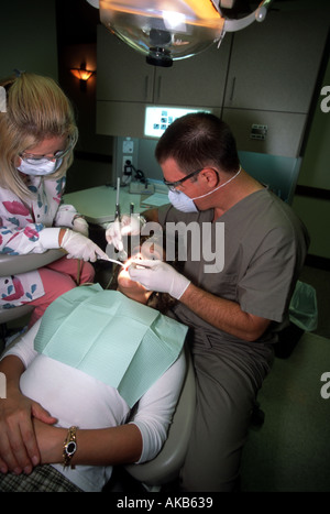 Regardant vers le bas sur un male dentist portant un masque de visage des gants en latex et des lunettes son assistante l'aide à effectuer Banque D'Images