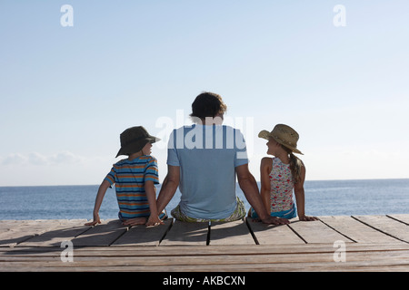 Son père et ses deux enfants (7-9) sitting on Jetty, vue arrière Banque D'Images
