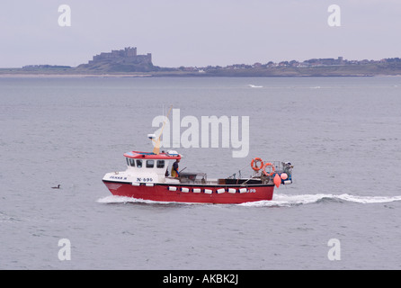 Un petit bateau de pêche près du port de l'Île Sainte de la côte de Northumberland avec château de Bamburgh en arrière-plan Banque D'Images