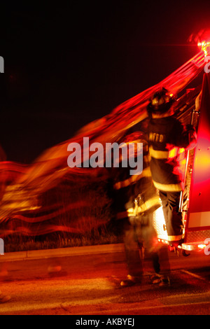 Deux pompiers de retirer le flexible de la pompe à incendie de nuit lors d'un appel d'urgence Banque D'Images