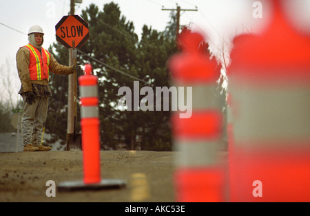 Roadworker lente holding signe avec cônes de construction en premier plan Banque D'Images