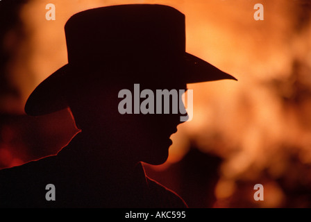 Young man wearing cowboy hat silhouetté par bonfire Banque D'Images