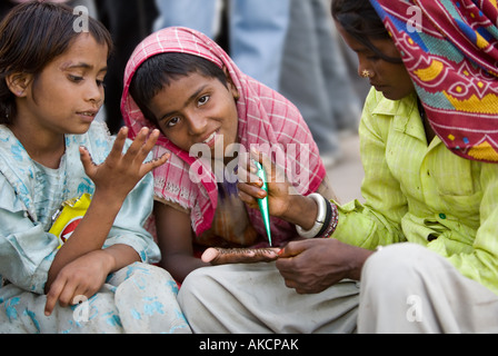 Une dame de l'Inde l'application d'un tatouage au henné à deux jeunes filles. La porte de l'Inde, Delhi, Inde. Banque D'Images