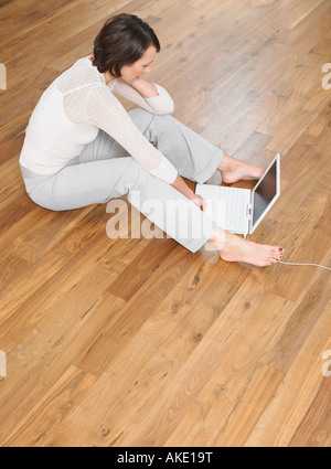 Femme était assise sur le plancher de bois à l'aide d'ordinateur portable Banque D'Images