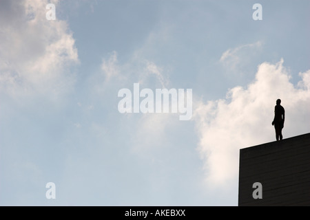 Antony Gormley sculpture, figure debout sur le bord du toit du bâtiment contre ciel nuageux ciel bleu, 'Event Horizon', London, England, UK Banque D'Images