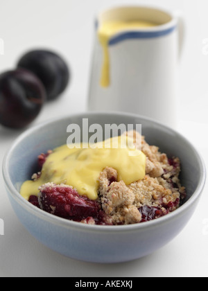 Un bol de crème anglaise et crumble de prunes sur fond blanc l'alimentation éditoriale Banque D'Images