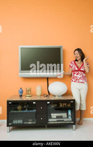 Jeune femme tenant une télécommande et près d'un cabinet Banque D'Images