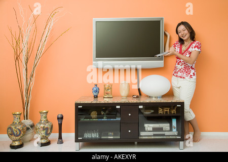 Jeune femme tenant une télécommande et près d'un cabinet Banque D'Images