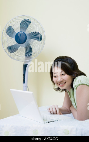 Portrait d'une jeune femme étendue sur le lit et à l'aide d'un ordinateur portable Banque D'Images