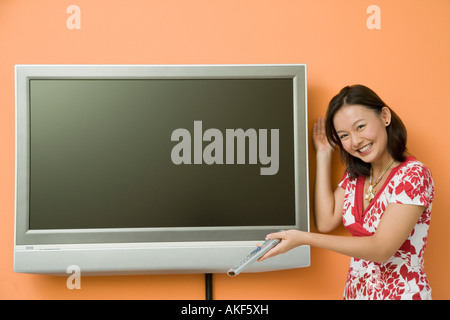 Portrait of a young woman holding a télécommande et smiling Banque D'Images