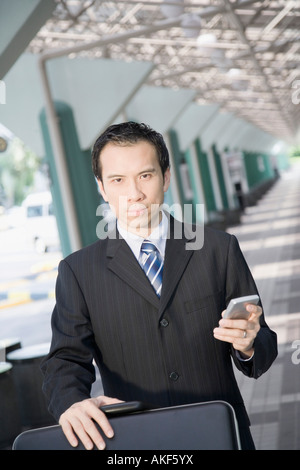 Portrait d'un homme d'affaires à l'aide d'un palmtop et en poussant un chariot à bagages Banque D'Images