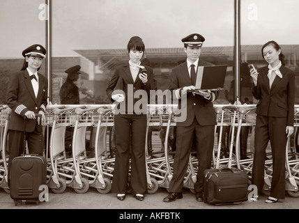 Deux femmes, l'équipage de cabine holding les téléphones mobiles et debout avec deux pilotes dans un aéroport Banque D'Images