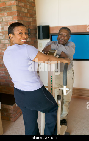 Les Seniors Américains africains exerçant sur la machine pas-à-pas et une télévision à écran plasma Banque D'Images