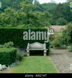 Pelouse à côté étroit chemin pavé menant au siège de pierre en face de l'if de clipsage en grande couverture country garden Banque D'Images