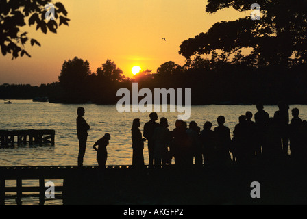 Personnes standing on jetty en regardant le coucher du soleil, Oulton Broad, Suffolk, Angleterre Banque D'Images