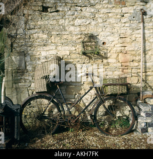 Vieux vélo noir avec panier et siège en osier childs appuyé contre un mur en pierre Banque D'Images