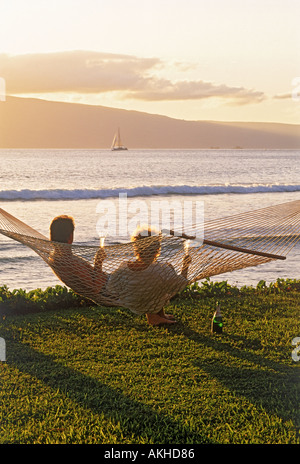 Couple sitting in hammock partager coucher de bouteille de champagne pour célébrer la bonne vie sur l'île de Maui Banque D'Images