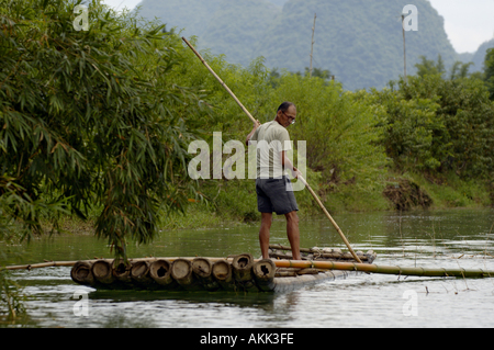 Homme debout sur un radeau en bambou et de l'aviron le long de la rivière Yulong, Yangshuo, Guangxi, Chine. Banque D'Images