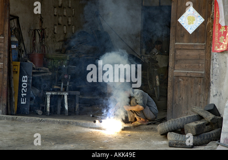 L'homme en vertu de brasage un nuage de fumée à la porte de son garage, Yangshuo, Guangxi, Chine. Banque D'Images