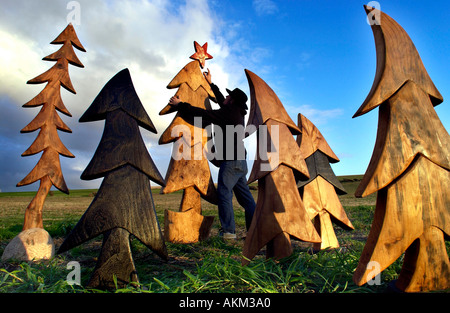 Sculpteur sur bois Johnny Woodford mettre une étoile rouge sur l'un de ses arbres de Noël gravé à la main, fabriqué à partir de l'orme. Banque D'Images