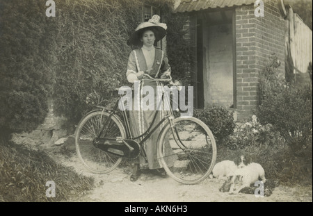 Carte postale photographique de la jeune femme avec les chiens de compagnie et de bicyclette dans son jardin vers 1910 Banque D'Images