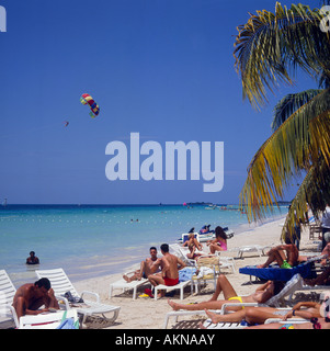 Les touristes européens se coucher et s'asseoir sur les chaises longues au bord de la mer à Negril Beach la côte ouest de la Jamaïque dans les Caraïbes Banque D'Images