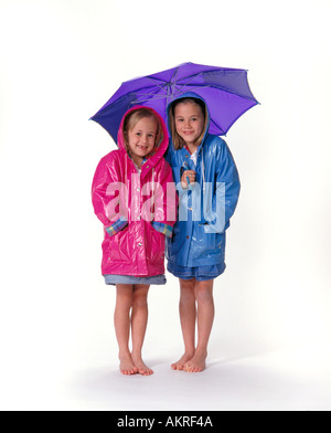 Deux jeunes filles avec des manteaux de pluie et un parapluie on white Banque D'Images