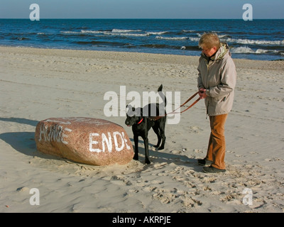 Femme avec un chien noir sur la plage d'un séjour d'une bordure de signer sur une pierre montrant fin de la zone autorisée pour les chiens Banque D'Images