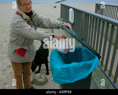 Femme avec un chien hybride noir Labrador Border Collie mix sur plage à Usedom disposer un sac en plastique avec la saleté de chien n'en levrette Banque D'Images