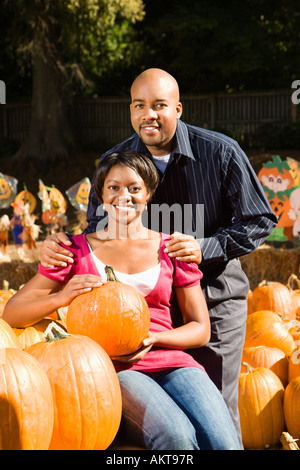 Portrait of happy smiling couple sitting in pumpkins at outdoor market Banque D'Images