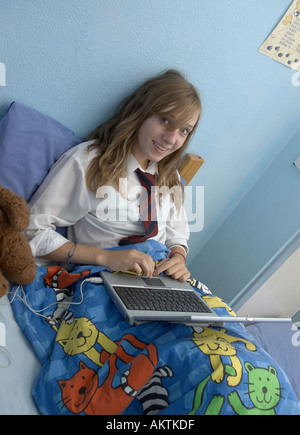 A smiling schoolgirl fait ses devoirs dans son lit sur un ordinateur portable Banque D'Images