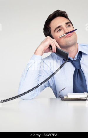 Businessman on phone balancing pen sur la lèvre supérieure Banque D'Images