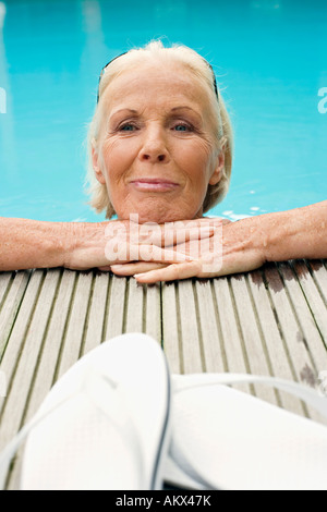 Allemagne, Senior woman resting on edge of pool, smiling Banque D'Images