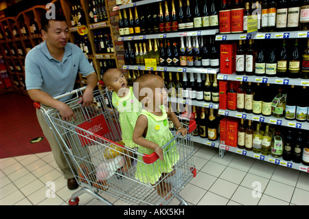 Un homme pushs panier avec ses deux filles jumelles à différents vins chinois dans un supermarché Carrefour à Beijing 22-Jul-06 Banque D'Images