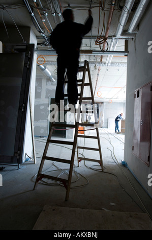 Travailleur de la construction travaille à des lignes de câble dans une enveloppe du bâtiment Banque D'Images