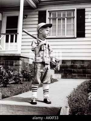 Jeune garçon posant en uniforme de baseball bat avec gant et en face de la maison en 1950 s Banque D'Images