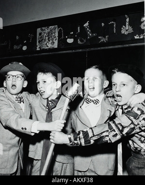 Quatre jeunes garçons à l'école faisant semblant de chanter dans des micro de 1950 s Banque D'Images