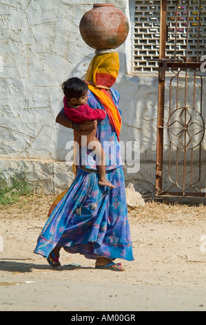 Une femme musulmane du Rajasthan avec une burqa couvrant son visage se dirige vers le puits du village avec son jeune fils sur sa hanche. Banque D'Images