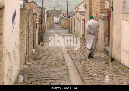 Un monsieur en pakistanais drerss traditionnels dans une ruelle pavée traditionnelle derrière des maisons mitoyennes dans le Lancashire un asiatique ar Banque D'Images