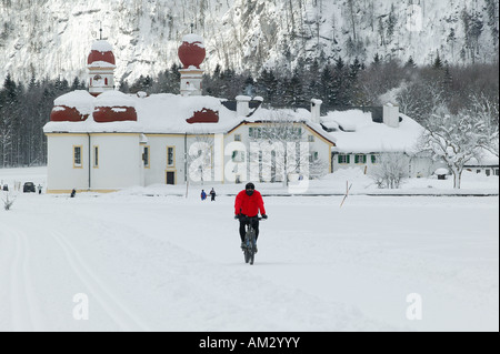 Église de Saint-Barthélemy à la Koenigssee, Mountainbiker passe au-dessus du lac gelé, Berchtesgaden-campagne, Haute-Bavière, Germ Banque D'Images