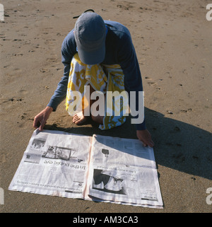 Man reading newspaper sur plage Tenby, Pembrokeshire au Pays de Galles du Sud Banque D'Images