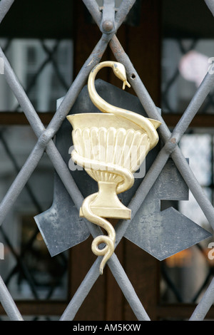 Gros plan d'un bol traditionnel de Hygieia, symbole du serpent et de la tasse, sur la grille en fer d'un magasin de pharmacie. Banque D'Images