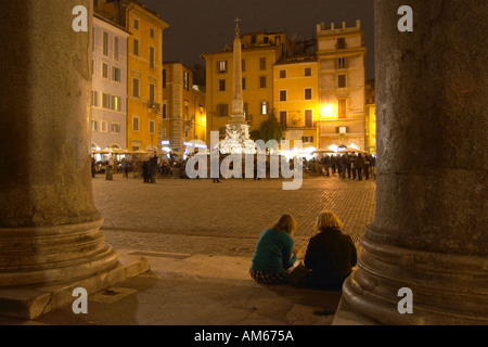 Le Panthéon de nuit. Deux personnes s'asseoir entre les colonnes et regarder la piazza. Piazza della Rotonda, Rome, Latium, Italie. Banque D'Images