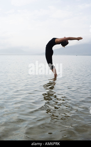 Woman doing a back bend Yoga pose debout dans l'eau Banque D'Images