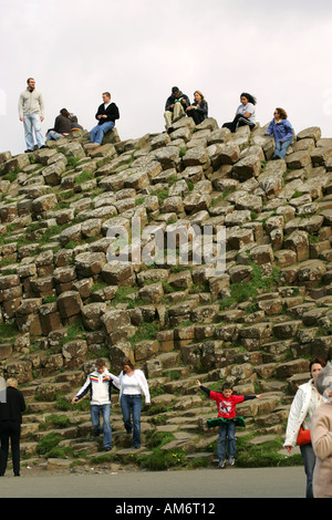 Les touristes grimper tout au cours de la forme hexagonale des pierres sur la Chaussée des géants d'Irelands premiere attraction touristique Co Antrim Banque D'Images