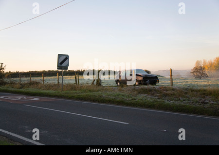 Épave de voiture abandonnée dans un champ. L'autre côté de la clôture. Le long de la route. Tôt le matin. Banque D'Images