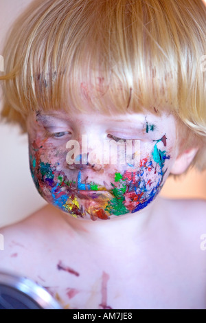 Effronté jeune avec face recouverte de peinture colorée à la recherche dans un miroir Banque D'Images